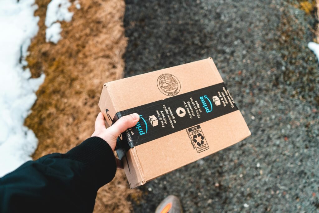 pexels-photo-16158539-16158539 A person holding a cardboard Amazon Prime package on a snowy urban sidewalk.
